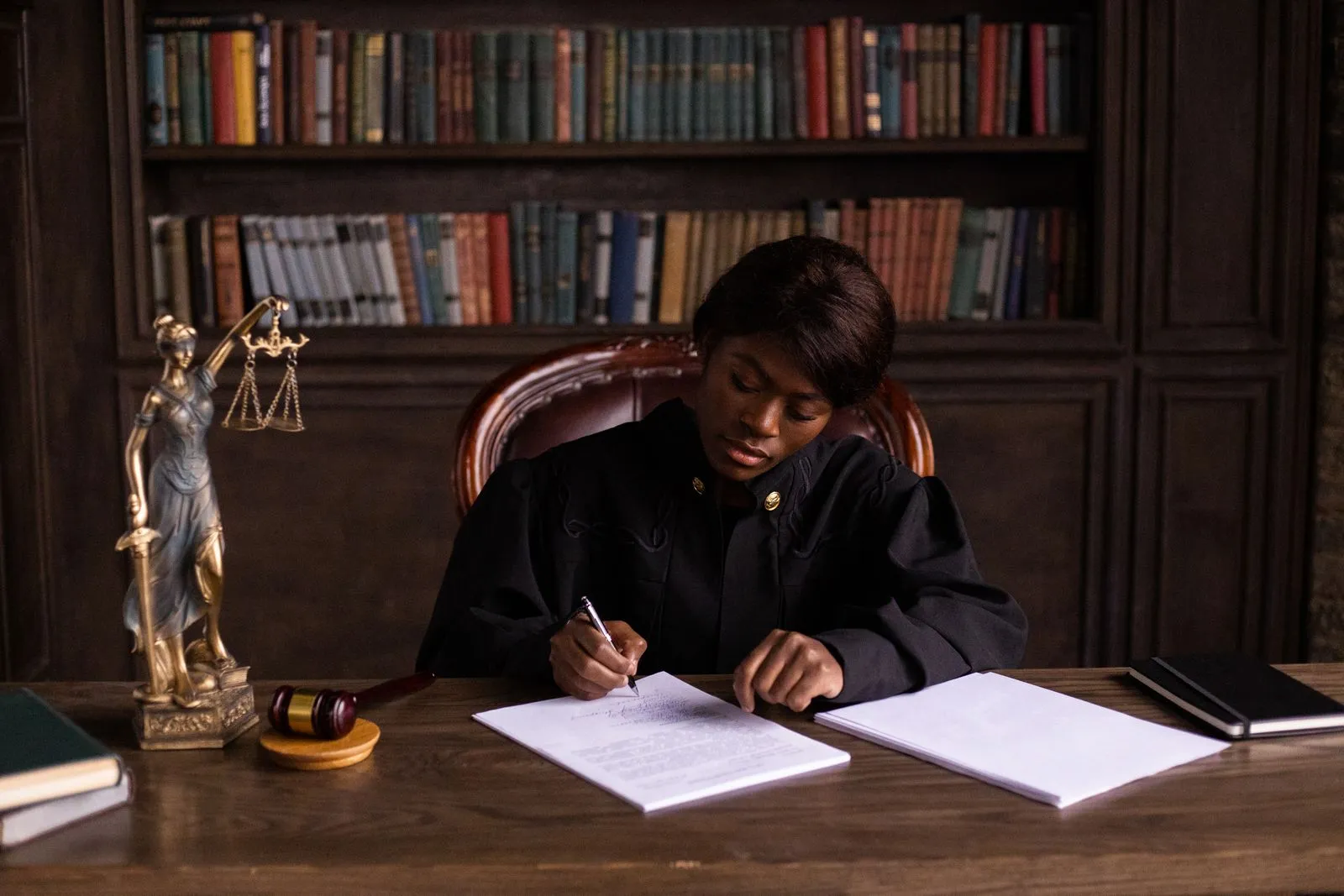 A judge writing on a document at a desk in an office library